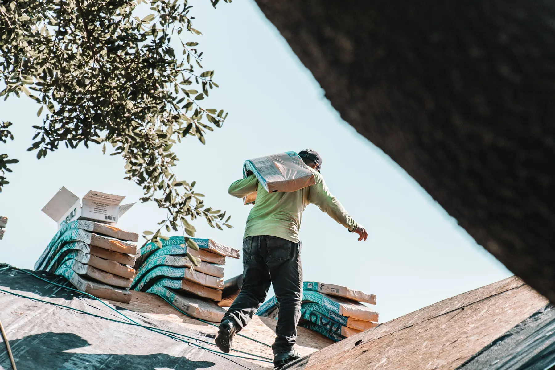 A roofer carrying a bundle of shingles across a roof